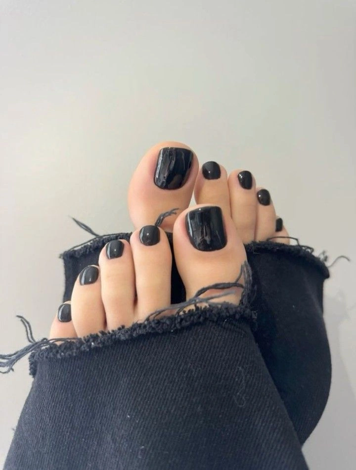 Короткі нігті на ногах у чорному глянці поруч із чорним денімом