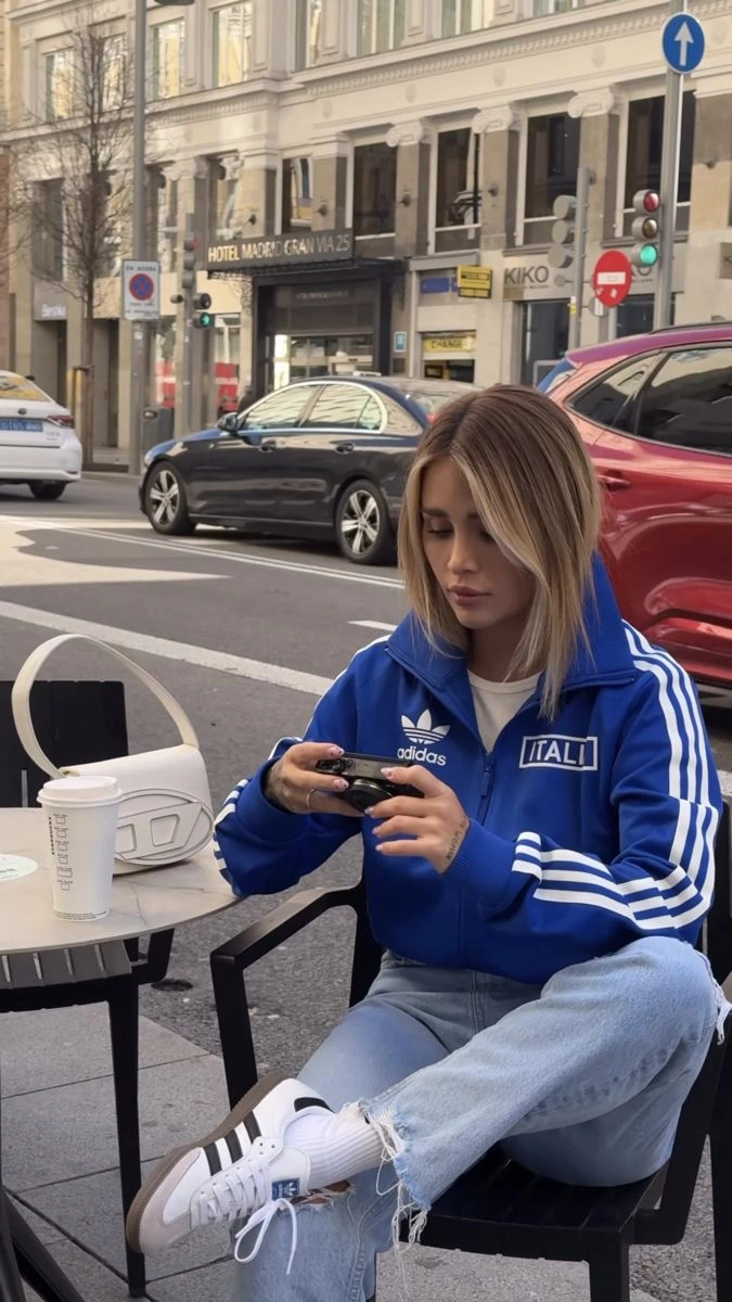 Яскраво-синя спортивна куртка з білими смужками й написом Italia, біла футболка, світлі рвані джинси й білі кеди