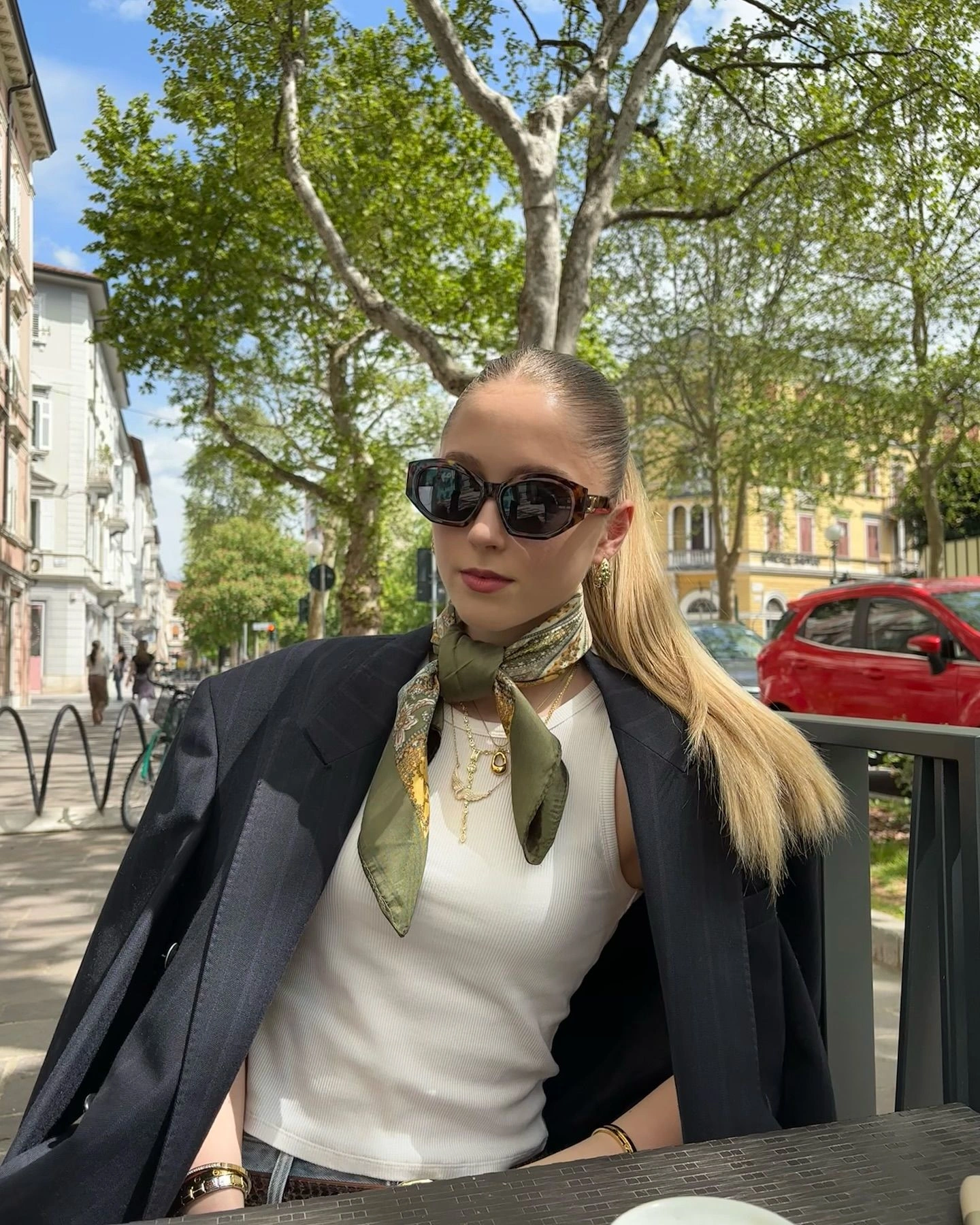 Оливкова хустка трикутником Оливкова хустка складена трикутником, гострі кути спадають на груди, біла майка й темний жакет на плечах